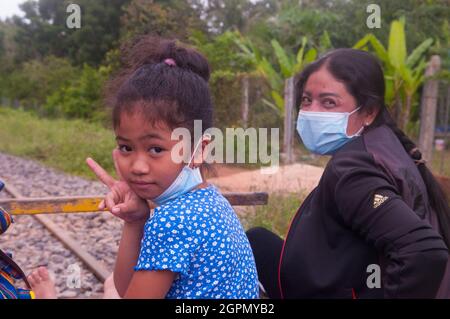 Eine kambodschanische Mutter und Tochter, beide mit schützenden Gesichtsmasken, reiten während der COVID-Pandemie von 19 auf dem Bamboo Train. Provinz Battambang, Kambodscha. September 2021. © Kraig Lieb Stockfoto