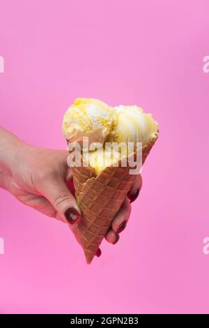 Eine Hand hält einen Eiskegel auf einem rosa Popsicle Hintergrund in einem Waffelbecher Stockfoto