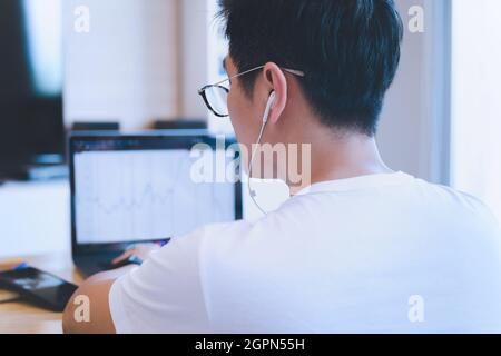 Rückansicht eines Traders mit Brillen, die zu Hause auf einem Laptop an den Aktienmarkt-Charts arbeiten. Stockfoto