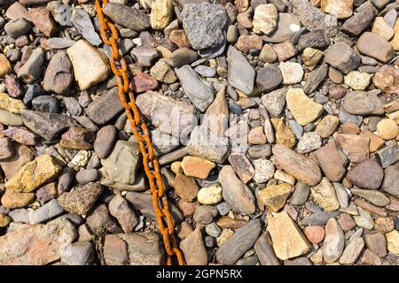 Eine alte rostige Kette auf einem Hintergrund von Felsen aller Farben bei Ebbe am Strand von Roscanvel, Finistere, Britanny, Frankreich. Stockfoto