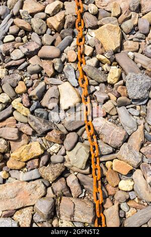 Eine alte rostige Kette auf einem Hintergrund von Felsen aller Farben bei Ebbe am Strand von Roscanvel, Finistere, Britanny, Frankreich. Stockfoto