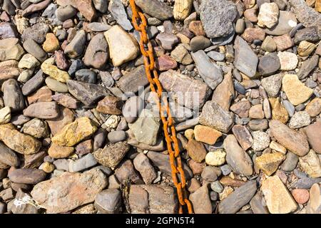 Eine alte rostige Kette auf einem Hintergrund von Felsen aller Farben bei Ebbe am Strand von Roscanvel, Finistere, Britanny, Frankreich. Stockfoto