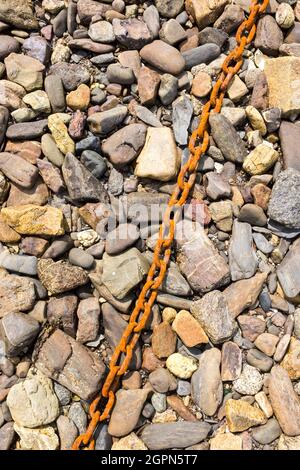 Eine alte rostige Kette auf einem Hintergrund von Felsen aller Farben bei Ebbe am Strand von Roscanvel, Finistere, Britanny, Frankreich. Stockfoto