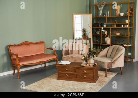 Hintergrundbild von eleganten Salon-Interieur mit bequemen Samt-Sofa und antiken Möbeln in Grüntönen Stockfoto
