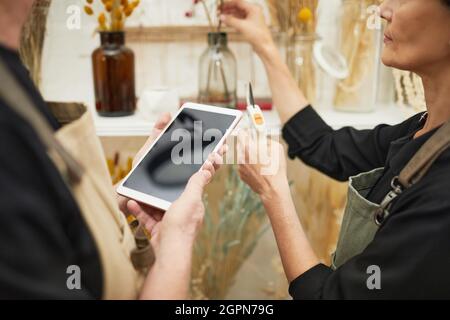 Nahaufnahme von zwei reifen Floristen mit Tablet während der Arbeit im Blumenladen Stockfoto