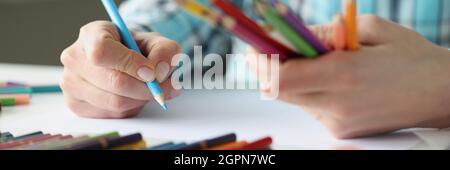 Weibliche Hände halten mehrfarbige Stifte und ein Blatt Papier liegt auf dem Tisch Stockfoto