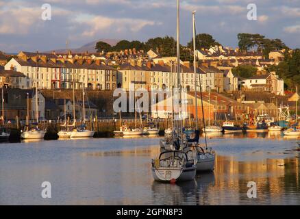 Boote im Hafen, Spiegelungen und farbenfrohe Terrassenhäuser entlang des Flusses Seiont kurz vor Sonnenuntergang in Caernarfon, Gwynedd, Wales Stockfoto