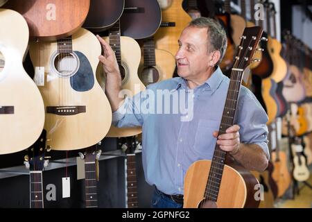 Der Mann steht in der Nähe von akustischen Gitarren im Musikgeschäft. Stockfoto