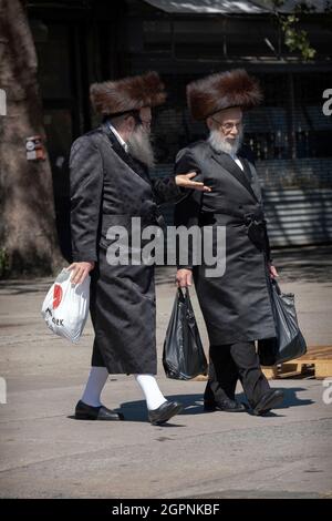 Zwei orthodoxe jüdische Männer, die traditionelle Shtreimel-Hüte tragen, laufen auf der Bedford Ave. Mit Einkaufstaschen. Auf Sukkos in Williamsburg, Brooklyn, New York Stockfoto