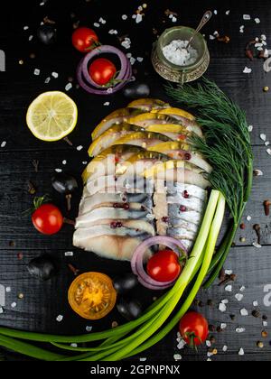 In Scheiben geschnittener Fisch, gesalzener Hering, geräucherter Makrele mit Kirschtomaten, grünen Zwiebeln, Dill, Zitrone und Gewürzen Stockfoto