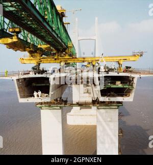 Eine Ansicht der Brückendeckereinheiten, die während des Baus des zweiten Severn Crossings installiert werden, zeigt eine speziell entwickelte Startbrücke über Kopf und zwei Arbeiter, die in einer der Deckeinheiten stehen. Die zweite Severn Crossing dauerte vier Jahre und war ein gemeinsames Tiefbauprojekt zwischen Laing Civil Engineering und dem französischen Unternehmen GTM. Die Arbeiten begannen im April 1992 und die Eröffnungszeremonie fand später am 5. Juni 1996 statt. Bei der Überfahrt handelt es sich um eine Kabelbrücke, die sich über 5000 Meter über den Fluss Severn erstreckt, der England und Wales verbindet, 3 Meilen stromabwärts Stockfoto