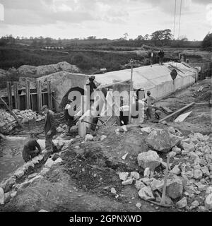 Ein Blick auf den Bau der Midland Link Autobahn, zwischen Junction 13 und Junction 11 der M6, zeigt ein Team von Arbeitern, die sich um einen Betonkulvert versammelten. Die Arbeiten am Midland Link-Abschnitt der Autobahn M6 zwischen Dunston und Shareshill (Junction 13 - Junction 11) wurden von der Bauingenieurabteilung der John Laing Construction Ltd. Durchgeführt. Die Autobahn wurde am 14. März 1966 für den Verkehr freigegeben. Stockfoto