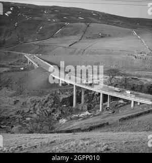 Ein Blick auf den Bau der Autobahn M6 durch die Lune Gorge, mit der Roger Howe Brücke im Vordergrund, die die A685 über den Fluss Lune führt, und dem Lawtland House Viadukt im Hintergrund, der die A685 über die Autobahn führt. Die Arbeiten am Abschnitt Lune Gorge der Autobahn M6 zwischen Killington und Tebay (Junction 37 - Junction 38) wurden von John Laing Construction Ltd. Durchgeführt. Die Arbeiten begannen im Oktober 1967 und die Autobahn wurde im Oktober 1970 für den Verkehr geöffnet. Die Strukturen in diesem Foto befinden sich an den Gitterreferenzen NY6129602758 und NY6116502666 in Richtung Süden Stockfoto