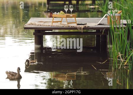 Tolle Zeit für ein Picknick auf dem hölzernen Pier mit Tischset mit Wein und Obst. Romantisches Date. Erholung und Reisen. Schöne Sommerabende.Tourismus und e Stockfoto