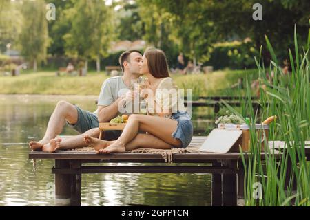 Verliebtes Paar küsst sich am Sommertag auf einem Picknick an einem wunderschönen Ort auf dem hölzernen Pier. Glück und Gelassenheit. Ruhe und Genuss .schöne Momente von Stockfoto
