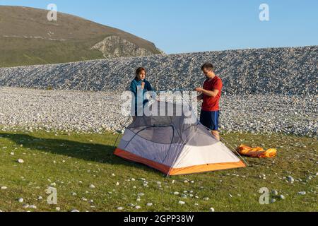 Junge kaukasische Touristen in Sportbekleidung, die ein Zelt auf einem Campingplatz inmitten von Felsen in der Natur aufschlagen Stockfoto