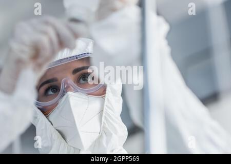 Arzt in einem Schutzanzug, einer medizinischen Maske und einer Brille, die den Katheter auf dem Fallzähler hält Stockfoto