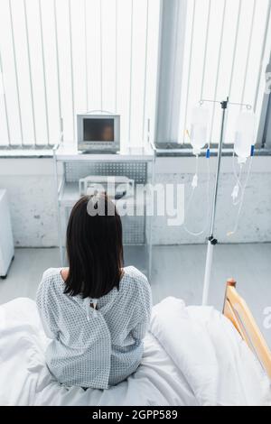 Rückansicht der Frau im Patientenkleid, die auf dem Krankenhausbett sitzt Stockfoto