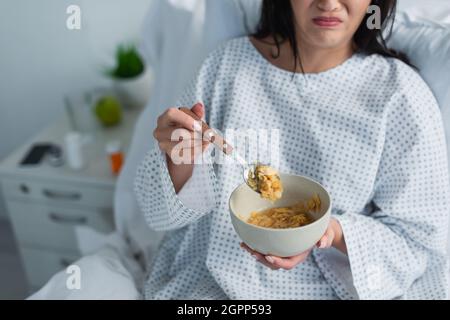 Teilansicht einer angewiderten Frau, die im Krankenhaus einen Löffel mit Maisflocken und eine Schüssel hält Stockfoto