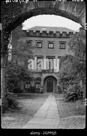 Wand mit Archway vor Nr. 9, The College, County Durham, 1942. Eine Außenansicht des St. Mary's College, heute bekannt als Choristerkollegium, von Norden aus durch einen Torbogen gesehen. Das ehemalige prägendale Haus, heute eine Schule, hat ein mittelalterliches Gewebe mit Veränderungen im 17. Und 18. Jahrhundert. Das Haupthaus hat drei Stockwerke und fünf Fenster mit Türmen an jeder Ecke. Die Brüstung ist umrastet. An der Rückseite des Gebäudes befindet sich der kurze Arm des L-förmigen Grundrisss. Der Bogen im Vordergrund ist Teil einer Gartenmauer mit Material aus dem Mittelalter, dem 17. Und 18. Jahrhundert. Die Wand kann früher sein Stockfoto