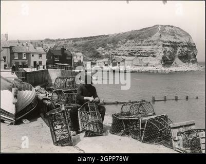 Seaton Garth, Staithes, Hinderwell, Scarborough, North Yorkshire, 1930er Jahre. Ein Mann, der Hummertöpfe am Strand neben Seaton Garth in Staithes mit der Cowbar NAB im Hintergrund ausbessert. Stockfoto