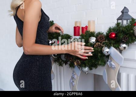 Verkürzte Ansicht der eleganten Frau in der Nähe des Kamins mit dekorierter Kieferngirlande und Kerzen Stockfoto