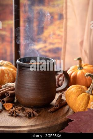 Dampfender Becher mit heißer Schokolade und Mini-Kürbissen an einem Fenster mit farbenfrohem Herbsthintergrund Stockfoto