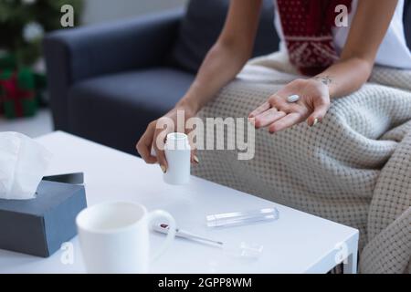 Beschnittene Ansicht einer kranken Frau mit Pille in der Hand in der Nähe des Thermometers und einer Tasse warmen Getränks auf einem verschwommenen Tisch Stockfoto