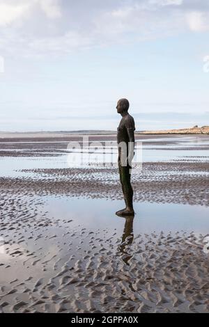 Eine Seite mit Blick auf eine Antony Gormley lebensgroße gusseiserne Skulptur „Another Place“ am Crosby Beach, Merseyside, Großbritannien bei Ebbe Stockfoto