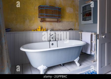 Wandschrank und Gummienten mit freistehender Badewanne in Suffolk Cottage. Stockfoto