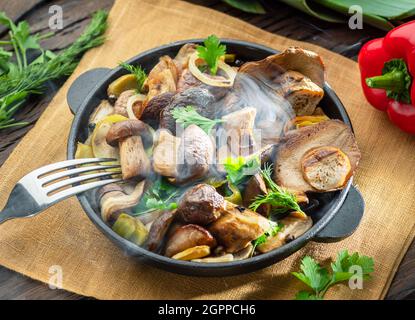 Garen Sie einfach dampfende Steinpilze in der Pfanne auf dem Holztisch. Draufsicht. Stockfoto