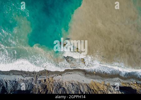 Luftaufnahme der Meeresoberfläche mit Wellen, schmutzigem Wasser und Küstenlinie Stockfoto