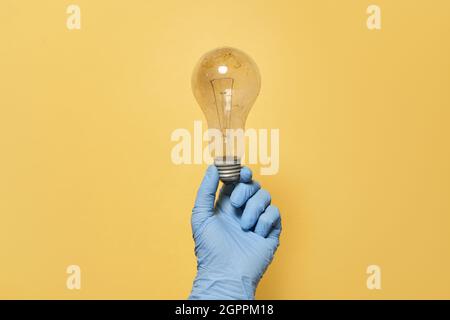 Elektrische Glühbirne in der Hand mit Latexhandschuh isoliert auf gelbem Hintergrund Stockfoto