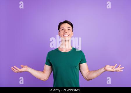 Foto von fröhlichen positiven jungen Mann heben die Hände leeren Raum Blick auf genießen isoliert auf violettem Hintergrund Stockfoto