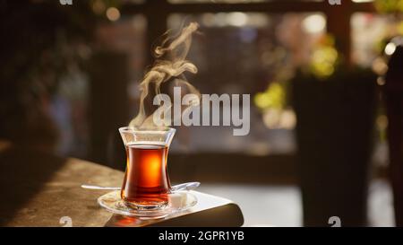 Dampfender türkischer Tee, serviert in tulpenförmigem Glas auf einer kleinen Untertasse auf dem Holztisch. Stockfoto