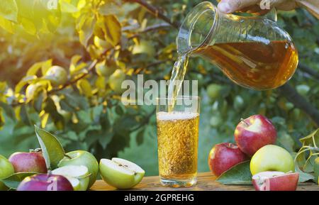 Apfelsaft in das Glas gießen. Frische Bio-Äpfel und ein Glas Apfelsaft auf einem Holztisch im Sommergarten. Stockfoto