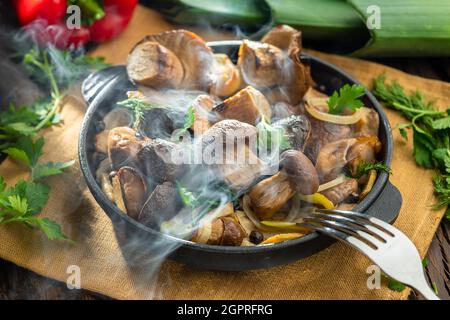 Garen Sie einfach dampfende Steinpilze in der Pfanne auf dem Holztisch. Draufsicht. Stockfoto