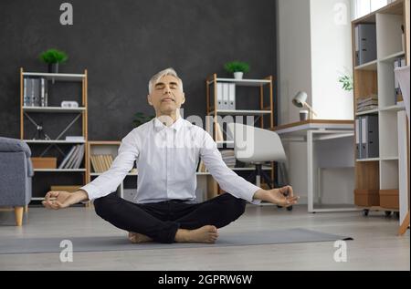 Entspannter Geschäftsmann meditiert in Lotusposition auf einer Sportmatte im Büro. Stockfoto