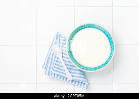 Griechischer Joghurt in blauer Schale, Leinenserviette und Holzlöffel auf weißem Tisch. Draufsicht Stockfoto