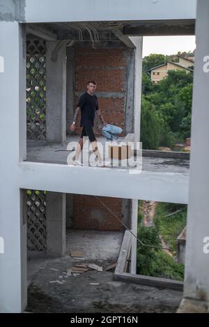 Ein junger, hübscher Kaukasusmann, der in lässiger Kleidung auf der verlassenen Baustelle herumläuft. Hochwertige Fotos Stockfoto