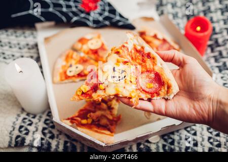 Helloween Pizza mit kleinen Papierkarren-O-Laternen-Kürbissen. Feiertagsfeier mit Kerzen und Kostümen. Halten Stück Pizza mit Halloween-Symbol auf fo Stockfoto