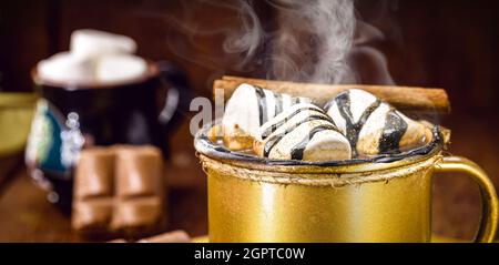 Heiße Schokolade mit Dampf oder Rauch in einer goldenen Tasse mit Marschmalchen und Zimt Stockfoto