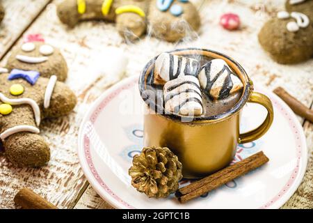 Heiße Schokolade mit Marschmalchen, Dampf oder Rauch, hausgemachtes Weihnachtsgetränk, mit mehreren Lebkuchenmännern auf dem Tisch Stockfoto