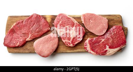 Verschiedene Steaks auf Holzschneidebrett - Streifenlende, Entrecote, Rumpsteak, Rinderfilet, isoliert auf weißem Hintergrund, Draufsicht Stockfoto