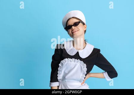 Junge Frau in Zimmermädchen-Uniform und stilvolle Sonnenbrille isoliert auf blauem Hintergrund Stockfoto