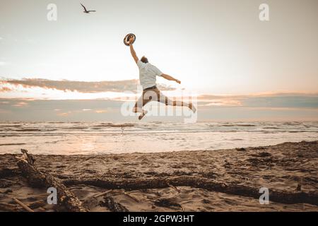 Fröhlicher Junge, der Sommerferien am Strand bei Sonnenuntergang genießt - junger Mann, der bei Sonnenaufgang am Strand springt - Urlaubskonzept Stockfoto