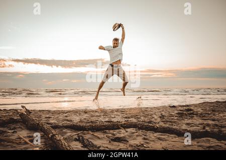 Fröhlicher Junge, der Sommerferien am Strand bei Sonnenuntergang genießt - junger Mann, der bei Sonnenaufgang am Strand springt - Urlaubskonzept Stockfoto