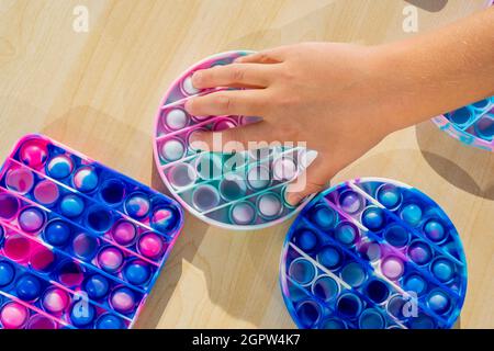 Kleines Kind spielt mit Anti-Stress sensorische Pop es an Holztisch. Hände halten und spielen popit Regenbogenfarbe. Trend des Jahres 2021. Draufsicht. Stockfoto