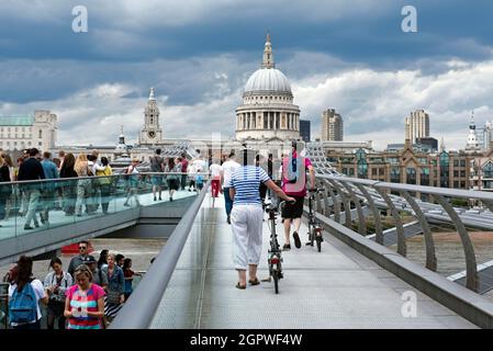 Menschen, die im Sommer die London Millennium Footbridge oder die Bridge über die Themse überqueren, schieben Fahrräder mit der St. Paul's Cathedral im Hintergrund. Stockfoto