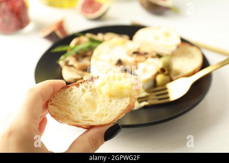 Die weibliche Hand hält die Brotscheibe mit Camembert, Nahaufnahme und selektivem Fokus. Stockfoto